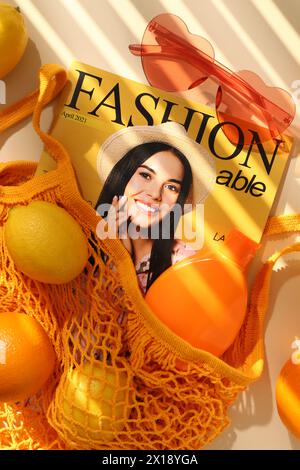 Sac à ficelle avec des fruits frais, magazine de mode et accessoires de plage sur fond beige, pose plate Banque D'Images