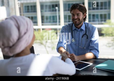 Un médecin caucasien portant une chemise bleue et un stéthoscope parle à un patient Banque D'Images