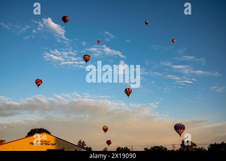 Une flotte de montgolfières vibrantes prend le ciel au-dessus d'un marché fermier local au coucher du soleil, ajoutant une touche de magie à la fin de la journée. Banque D'Images