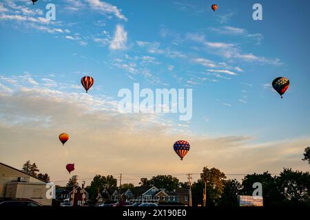 Une flotte de montgolfières vibrantes prend le ciel au-dessus d'un marché fermier local au coucher du soleil, ajoutant une touche de magie à la fin de la journée. Banque D'Images