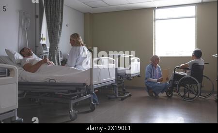 Vue latérale du Caucasian female doctor en interaction avec des patients de race blanche qui est au lit dans la paroisse à l'hôpital. Infirmière de race mixte en hijab Banque D'Images
