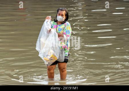 SAMUT PRAKAN, THAÏLANDE, 11 février 2024, Une femme avec un sac en plastique patère dans une rue inondée Banque D'Images