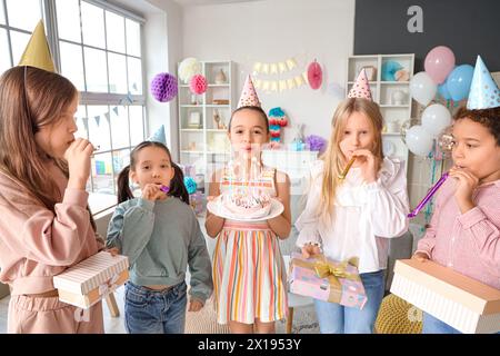 Mignonne petite fille soufflant des bougies sur le gâteau d'anniversaire avec ses amis à la fête à la maison Banque D'Images