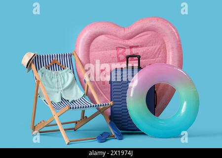 Matelas de natation en forme de coeur, anneau gonflable et valise sur fond bleu Banque D'Images