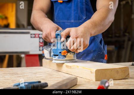 Close up d'un jeune homme builder carpenter égale avec une planche en bois vernis orbite aléatoire sander dans l'atelier Banque D'Images