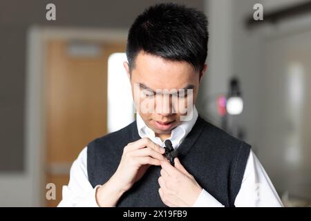 Un tuteur asiatique ajuste son micro-cravate pour un cours en ligne sur vidéo dans le studio d'enregistrement Banque D'Images