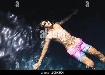 Un adolescent asiatique flotte dans l'eau dehors à la maison, portant des lunettes de soleil, espace de copie Banque D'Images