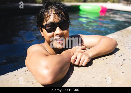 Adolescent asiatique se relaxant dans une piscine à la maison, portant des lunettes de soleil Banque D'Images