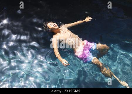Un adolescent asiatique flotte dans une piscine à l'extérieur à la maison, portant un fond de bain rose, espace copie Banque D'Images