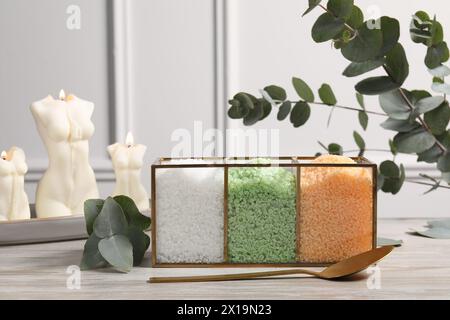 Différents types de sel de mer, cuillère, bougies et branches d'eucalyptus sur table en bois Banque D'Images