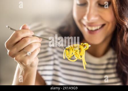 La jeune femme aime manger des spaghettis. Il a des pâtes Aglio e Olio tordues sur sa fourchette. Banque D'Images
