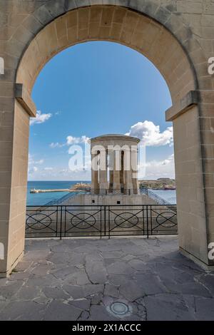 Le Mémorial de guerre de la cloche de siège encadré par une arche des jardins inférieurs de Barrakka, la Valette, Malte Banque D'Images