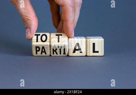 Symbole total ou partiel. Homme d'affaires tourne de beaux cubes en bois et change le mot partiel à Total. Belle table grise fond gris. Busines Banque D'Images
