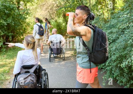 Un groupe diversifié d'amis par une journée ensoleillée dans le parc, y compris des personnes utilisant des fauteuils roulants et une femme avec une prothèse de jambe. Banque D'Images