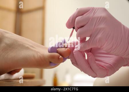 Pédicuriste professionnel peignant les ongles des orteils du client avec du vernis dans le salon de beauté, gros plan Banque D'Images