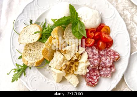 Cuisine italienne traditionnelle servie sur une assiette, fromage salami, herbes, baguette, tomates, Banque D'Images