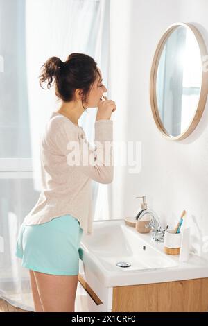 Une femme brune se brosse les dents devant un miroir de salle de bain le matin Banque D'Images