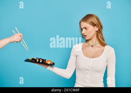 Une belle femme blonde tient délicatement une assiette de sushis, mettant en valeur l'art de la cuisine japonaise, les baguettes. Banque D'Images