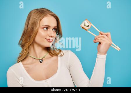 Une superbe femme blonde tient délicatement une paire de baguettes, mettant en valeur sa grâce et son calme. Banque D'Images