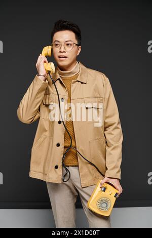 Un jeune homme à la mode dans une veste bronzée s'engage activement avec un téléphone jaune. Banque D'Images
