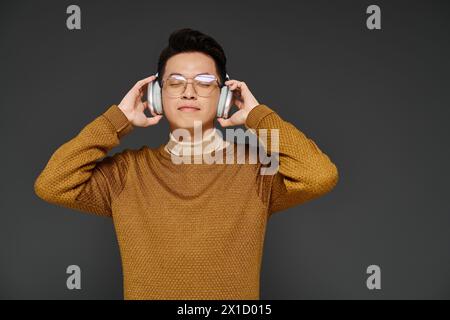 Un jeune homme élégant dans une tenue élégante écoutant attentivement à travers des écouteurs tout en portant des lunettes. Banque D'Images