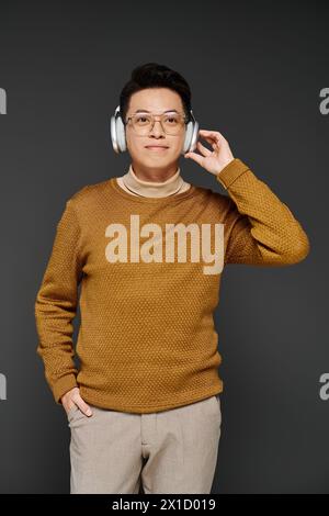 Un jeune homme à la mode dans un pull confortable écoute attentivement à travers des écouteurs élégants, exsudant la confiance sereine. Banque D'Images