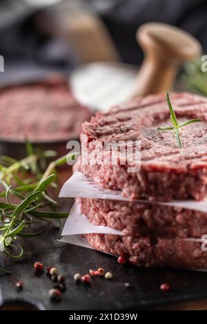 Patties de bœuf haché cru frais avec sel de romarin et poivre préparées sous forme de viande sur une planche à découper. Banque D'Images