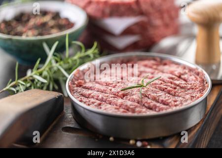 Patties de bœuf haché cru frais avec sel de romarin et poivre préparées sous forme de viande sur une planche à découper. Banque D'Images