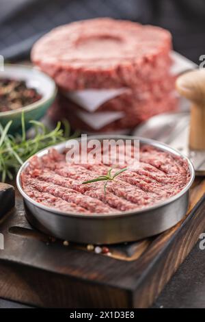 Patties de bœuf haché cru frais avec sel de romarin et poivre préparées sous forme de viande sur une planche à découper. Banque D'Images