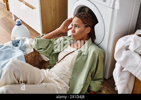 Femme afro-américaine avec des tresses afro est assis près de la machine à laver faisant la lessive dans une salle de bain. Banque D'Images