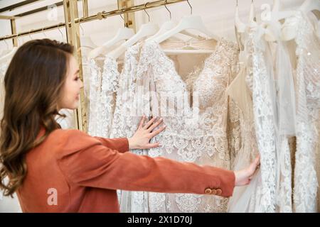 Une jeune belle mariée examine soigneusement un rack de robes de mariée dans une boutique de mariée. Banque D'Images