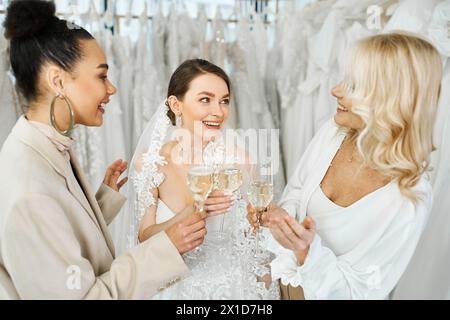 Une jeune mariée dans une robe de mariée, sa mère d'âge moyen, et sa meilleure amie en tant que demoiselle d'honneur se tiennent ensemble tenant des verres à champagne. Banque D'Images