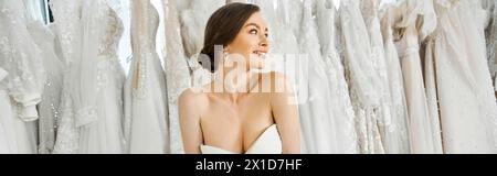 Une jeune, belle mariée brune se tient parmi un rack de robes de mariée blanches dans un salon de mariée. Banque D'Images