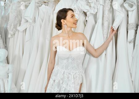 Une jeune mariée brune debout parmi une variété de robes dans un salon de mariage. Banque D'Images