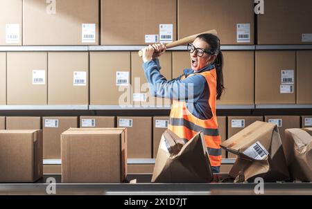 Ouvrière rebelle agressive brisant des boîtes au travail, elle est frustrée et en colère Banque D'Images