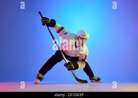 Homme ambitieux, joueur de hockey posant avec un bâton, montrant sa détermination sur fond bleu dégradé dans la lumière néon Banque D'Images