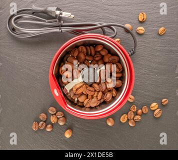 Un moulin à café électrique avec grains de café sur pierre d'ardoise, macro, vue de dessus. Banque D'Images