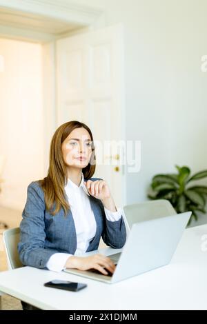 Femme professionnelle concentrée travaille avec diligence sur son ordinateur portable, son espace de travail baigné de lumière naturelle. Banque D'Images