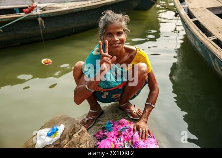 Femme lève le signe de la paix tout en lavant un vêtement dans le fleuve Gange à Varanasi, en Inde. Banque D'Images