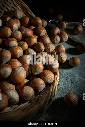 Noisettes en coquilles dans un panier en osier sur base d'ardoise avec casse-noix Banque D'Images