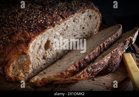 Pain de levain ensemencé en tranches en gros plan sur planche à découper en bois avec couteau vintage Banque D'Images