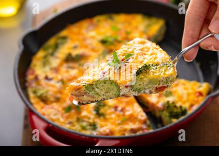 Tranche saine de frittata ou de quiche au brocoli et au poivron rouge, garnie de cheddar et de bacon cuit dans une poêle en fonte Banque D'Images