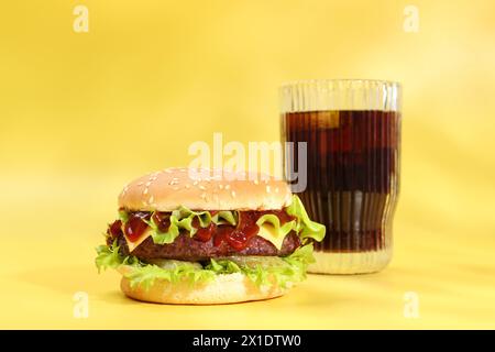 Hamburger avec délicieuse patty et boisson gazeuse sur fond jaune Banque D'Images