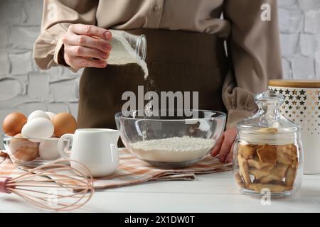 Femme ajoutant de la levure chimique dans un bol à la table en bois blanc, gros plan Banque D'Images