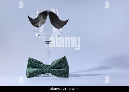 Visage de l'homme fait de moustache artificielle, noeud papillon et verre de vin sur fond bleu clair. Espace pour le texte Banque D'Images