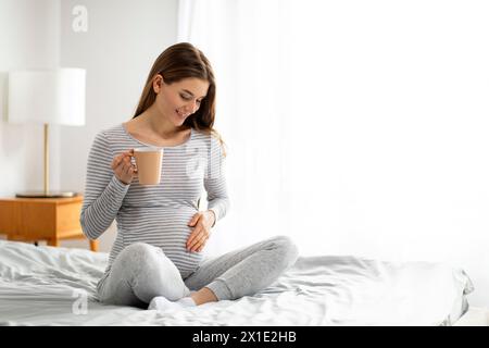 Femme enceinte profitant d'une tasse de thé au lit Banque D'Images