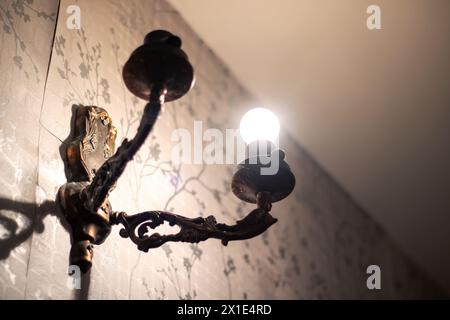 Une lampe jette une ombre sur le papier peint floral, créant des teintes et des nuances sur le mur. Le plafonnier en bois ajoute une touche artistique à la pièce à dar Banque D'Images