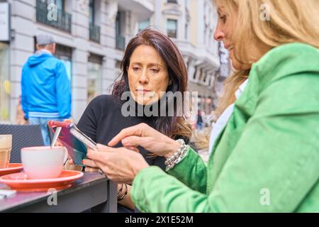 Deux filles dans un café, souriant, bavardant, buvant du café, regardant un smartphone Banque D'Images