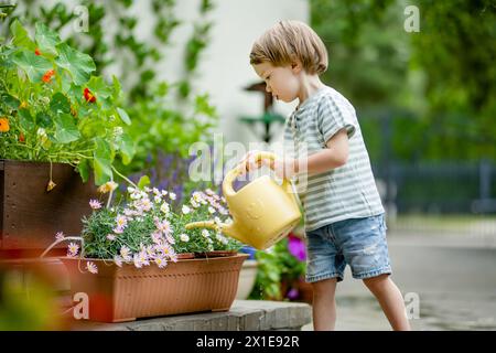 Mignon petit garçon arrosant des parterres de fleurs dans la cour arrière le jour d'été. Enfant utilisant l'arrosoir pour arroser les plantes. Enfant aidant avec les corvées quotidiennes. Maman Banque D'Images