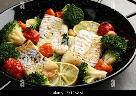 Morue savoureuse cuite avec des légumes dans une poêle sur une table grise, gros plan Banque D'Images